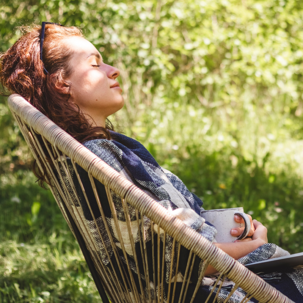 Žena odpočívá v křesle na zahradě s hrnkem v ruce